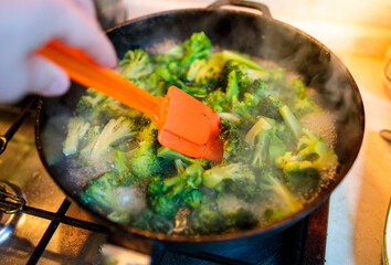 broccoli is stirred with an orange spatula in a cast iron skillet close-up