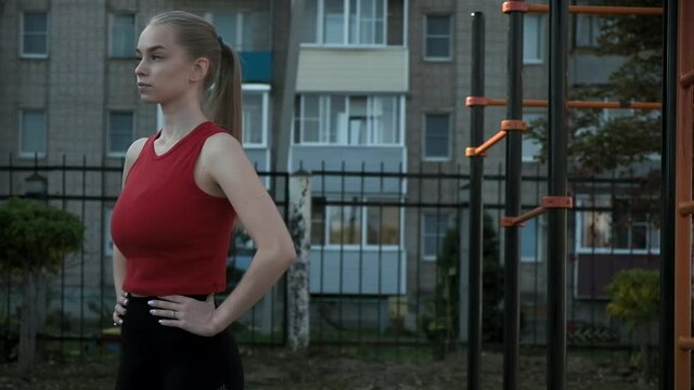 young fit blond busty woman with ponytail in red top exhales at sports ground