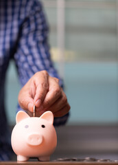 Vertical business man hand putting coins into the piggy bank, saving money concept.