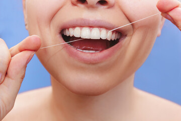 A cropped shot of a young beautiful woman flossing her teeth on a blue background. Close-up. Dental concept	