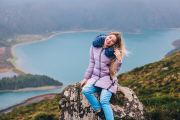 Naklejka premium a girl sits on a mountain, the wind develops her hair, A landscape view of the Lagoa do Fogo caldera under a foggy sky with great depth.