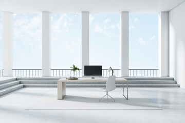 Computer on a desk standing in the middle of an empty bright room with columns and big windows, concrete floor, daylight. Real estate and interior design concept, 3d rendering