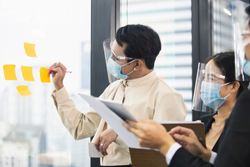 Asian office worker wearing face mask and face shield protect against writing on glass board, brainstorming thinking planning of business people. - Powered by Adobe