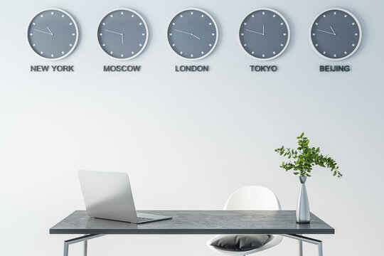 Time of world cities on wall clock in modern office space with dark marble table surface, laptop and green plane in glass vase