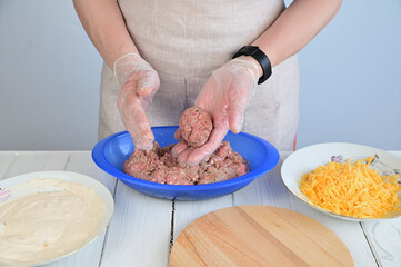 A woman in transparent gloves holds a rolled minced meat cutlet in her left hand