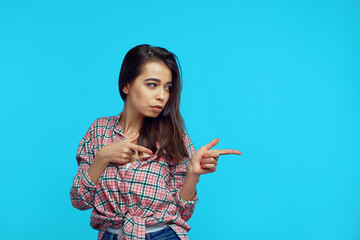 Attractive girl pointing with both hands at right blank space, standing against blue background
