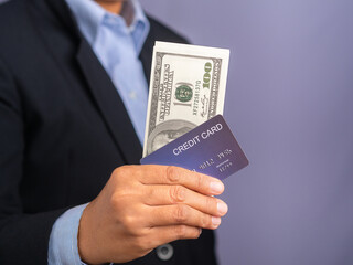 A young man holding a mockup blue credit card and US banknotes while standing in a studio. Close-up photo. Business and finance concept