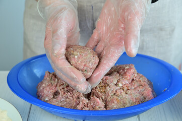 A woman holds a minced meat cutlet in her hands. Leftover minced meat is in a blue plastic bowl