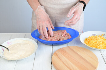 A woman in transparent gloves separates a lump of minced meat from the total mass in order to mold a cutlet