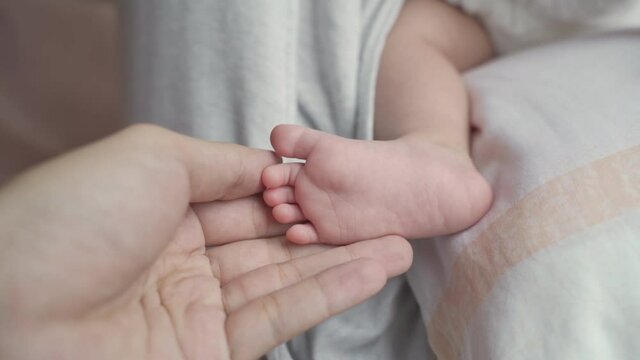 male father hand touching newborn baby infant foot with care and protection. small tiny feet closeup.
