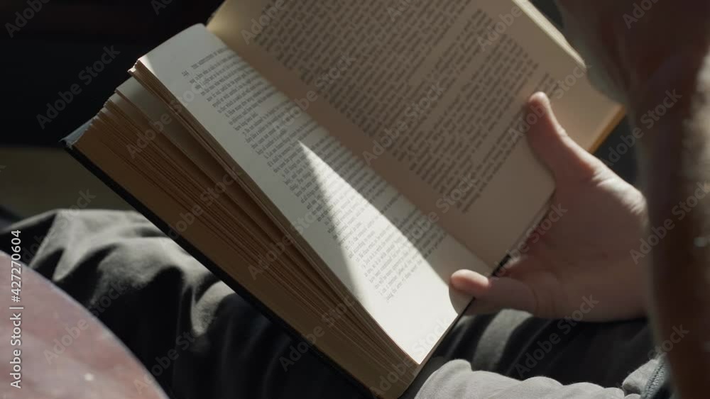Poster man drinking coffee while reading a book near a window with natural lighting