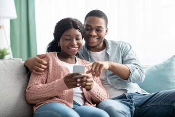 Happy black couple checking new shopping application on smartphone
