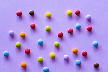 Multicolored chocolate candy smarties on purple background.