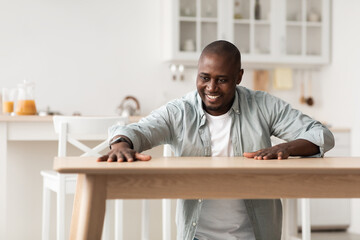 Happy african american man touching new wooden table, feeling pleasure of installing desk by yourself