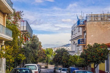 Residential street in historical Plaka district of Athens Greece  around slopes of Acropolis known as the Neighborhood of the Gods with cars parked and oranges on trees.