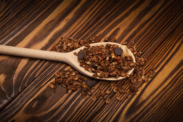 Chocolate granola cereal with nuts in a wooden spoon.