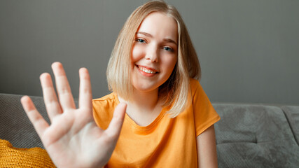 Happy woman portrait wave by hand greeting web camera view. Young beautiful woman talking hi by video call using while sitting on sofa in living room. Remote communication. Long web banner © Beton Studio