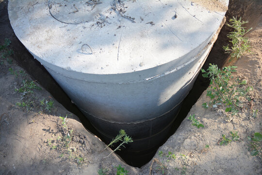 Installation of a septic tank made of concrete rings. Concrete sewer well, manhole rings installation into a square hole.