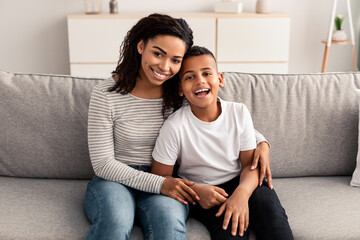 Portrait of black mother and son hugging on couch