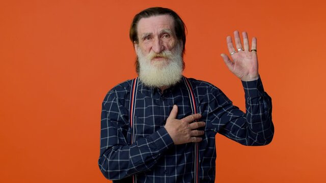 I swear to be honest. Sincere responsible senior old bearded gray-haired man raising hand to take oath, promising to be honest and to tell truth, keeping hand on chest. Elderly grandfather pensioner