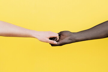 White hand and black hand clasped on yellow background