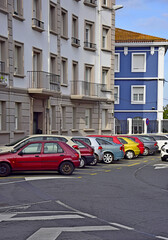 Fotografía casual de coches de diversos colores aparcados con el fondo de dos edificios también bastante coloridos