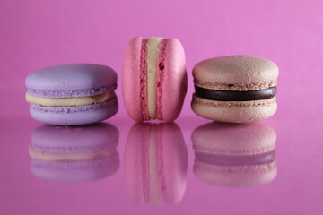 Three macaroons lilac brown chocolate lavender pink lie in a row on a pink fuchsia-colored background with reflection and a place for text and copyspace