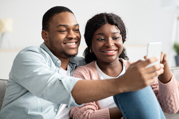 Cheerful african american couple taking selfie, using smartphone