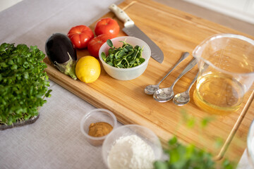selective focus. Kitchen table and wooden board with ingredients for cooking healthy food, salad of tomato, eggplant, onion, microgreen peas and sunflower. dressing with lemon juice