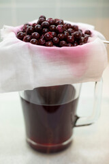 Straining 5 month soaked in gin sloe berries through muslin cloth to produce homemade sloe gin