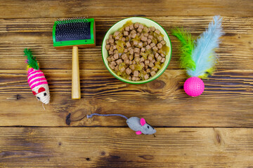Obraz na płótnie Canvas Canned cat food in bowl, cat toys and pet slicker brush on wooden background. Top view. Pet care concept
