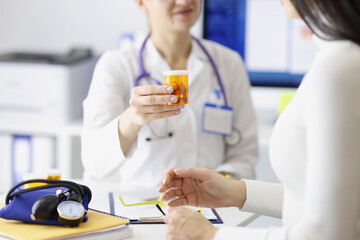 Doctor giving jar of medicines to young woman in clinic closeup