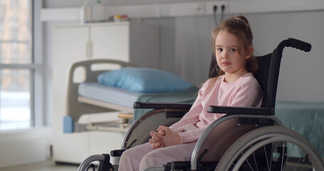 Sad little girl in a wheelchair in hospital ward looking at camera.