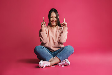 Asian excited woman pointing finger upward while sitting on floor