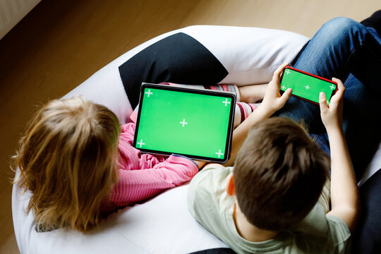 Kid boy and little girl gaming or using social media on mobile phone and tablet with chroma key background. Two children holding smartphone and laptop with green screen for commerce, new app
