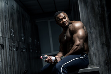 Fototapeta na wymiar Muscular african male in locker room. Man having rest after heavy training. Portrait of bodybuilder.