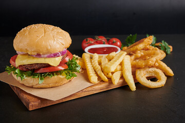 Homemade hamburger or burger with fresh vegetables and cheese lettuce and mayonnaise served, French fries on pieces of brown paper on black stone table . concept of fast food and junk food
