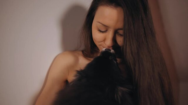 Close view: Funny little spitz dog kissing young nudist woman
