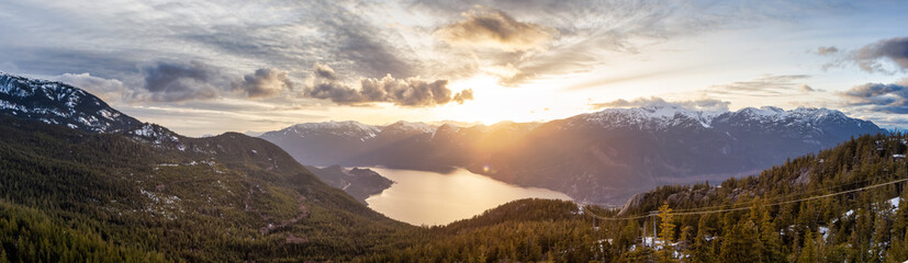 Naklejka na ściany i meble Panoramic View of Canadian Nature Mountain Landscape from Sea to Sky Gondola Summit Viewpoint. Colorful Sunny Spring Sunset. Taken near Squamish, North of Vancouver, BC, Canada.