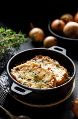 Onion soup with cheese croutons in a cast iron dish on a dark background. A traditional dish of French cuisine