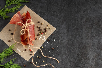 Homemade food. Herbs, spices and coarse salt. Healthy slices of spicy jerky tied with twine on parchment paper against a dark background. Copy space