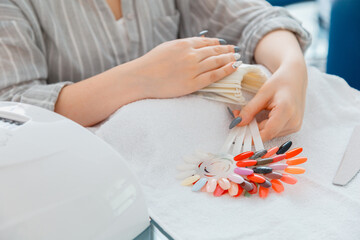 Female hands with artificial acrylic nails picks up new nail polish color during manicure procedure. Colored nail polish process on manicure in beauty salon. Hygiene and beauty of hands in nail salon