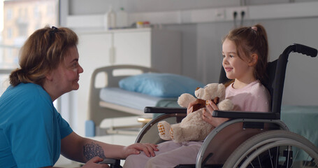 Child patient in wheelchair sitting in hospital ward talking to female nurse - Powered by Adobe