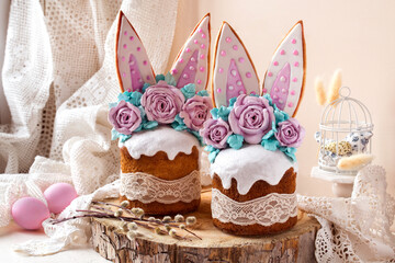 easter cake decorated with rabbit ears and roses meringue flowers on a light background on a wooden saw and willow branches