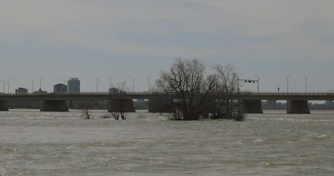 Ottawa River waters flooding over the islands with the high rise buildings of Ottawa and the Champlain Bridge in the background. 