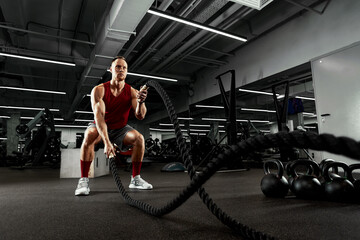 Sport. Strong man exercising with battle ropes at the gym with. Athlete doing battle rope workout at gym. Dramatic sports background.