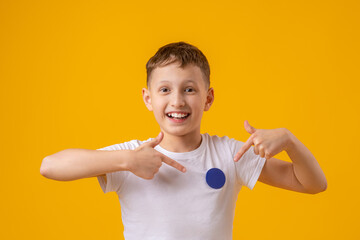 cheerful, happy child points his finger at the inscription on his white T-shirt, copying the place for the text. Smiling, the teenager shows off the badge. Advertising concept.