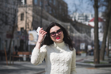 Young cheerful stylish woman using cell phone and texting message on city street