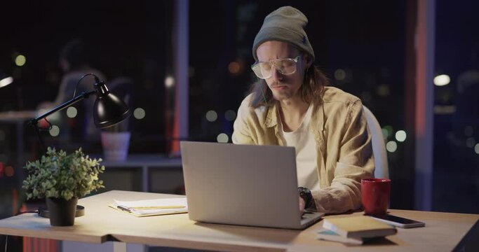 Caucasian hioster young creative designer desginging a project digital laptopp computer working from ocorporate office alone at night.