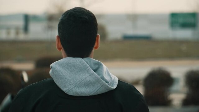 Hombre con chaqueta negra y capucha gris caminando de espaldas , hombre de cabello negro caminando hacia su motocicleta